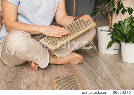 A woman sits on the floor with a wooden sadhu board with nails. Practice standing on nails. Indian Practices A woman sits on the floor with a wooden sadhu board with nails. Practice standing on nails. Indian Practices 86613270