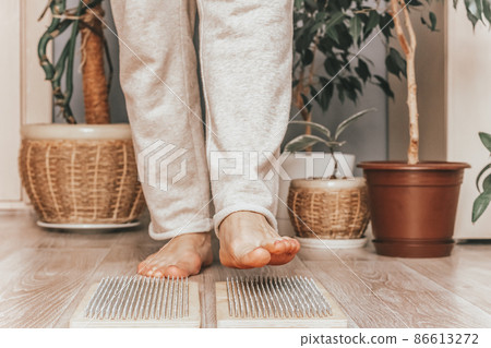 Woman stands on nails against background of home interior green plants. The practice of standing on nails. Woman stands on nails against background of home interior green plants. The practice of standing on nails. 86613272