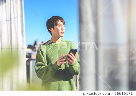 That young man operating a smartphone was on the balcony at home That young man operating a smartphone was on the balcony at home 86616171