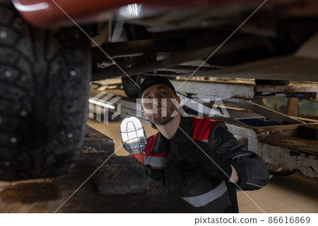 Mechanic Inspecting Car on Lift in Workshop Mechanic Inspecting Car on Lift in Workshop 86616869