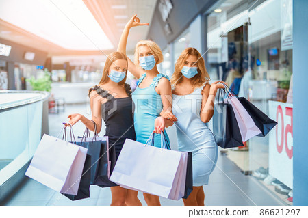 Funny Girlfriends in face mask holds shopping bags while walking in shopping mall. Covid-19 outbreak Funny Girlfriends in face mask holds shopping bags while walking in shopping mall. Covid-19 outbreak 86621297