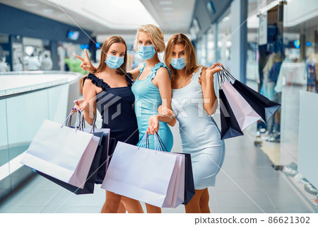 Girlfriends in face mask holds shopping bags while walking in shopping mall. Covid-19 outbreak 86621302