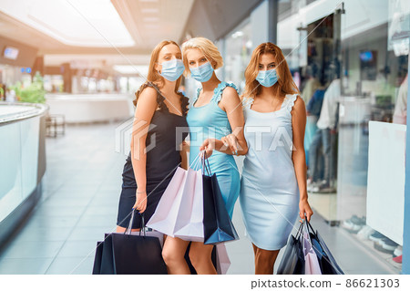 Happy women in face mask holds shopping bags while walking in shopping mall. Covid-19 outbreak 86621303
