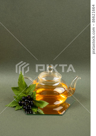 Black currant tea. Transparent glass teapot and black currant berries on a green background. Calming drink concept Black currant tea. Transparent glass teapot and black currant berries on a green background. Calming drink concept 86621664