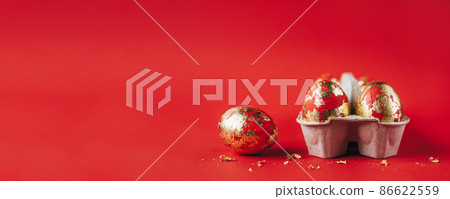Group of golden colored and decorated with sparkles Easter eggs in cardboard egg-box, Easter egg hunt celebration, colorful still life in paper box on red background. Copy space. 86622559