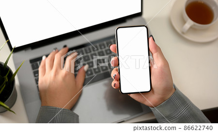 Top view, Businesswoman hands typing on laptop keyboard and holding smartphone Top view, Businesswoman hands typing on laptop keyboard and holding smartphone 86622740