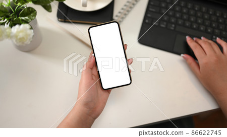 Female worker holding a smartphone and working on tablet Female worker holding a smartphone and working on tablet 86622745