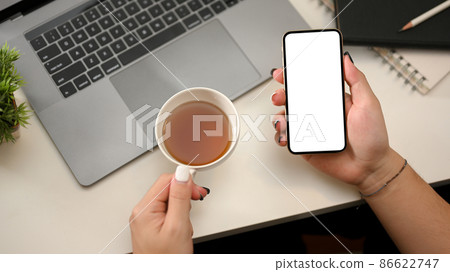 Modern office table with woman hands holding teacup and smartphone 86622747