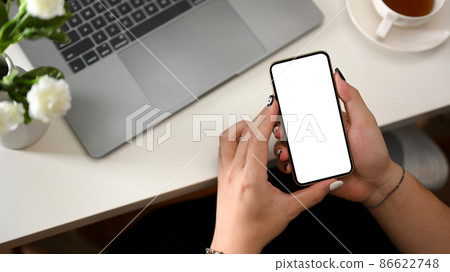 A female holding a mobile phone white screen mockup over workspace. 86622748