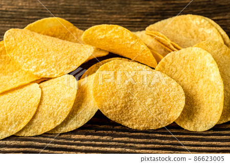 Potato chips on a wooden background. Salty crisps scattered on a table. 86623005