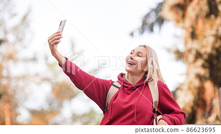 Attractive smiling woman with a backpack taking a selfie with her mobile outdoor in autumn, selective focus, format photo 16x9 Attractive smiling woman with a backpack taking a selfie with her mobile outdoor in autumn, selective focus, format photo 16x9 86623695