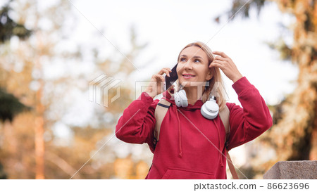 Using mobile outdoor. Attractive happy woman talking on a cellphone in an autumn urban park, selective focus, format photo 16x9 Using mobile outdoor. Attractive happy woman talking on a cellphone in an autumn urban park, selective focus, format photo 16x9 86623696
