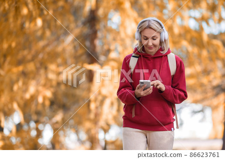 Typical caucasian woman in headset go through the park and hanging in her mobile, outdoor in autumn, selected focus. 86623761