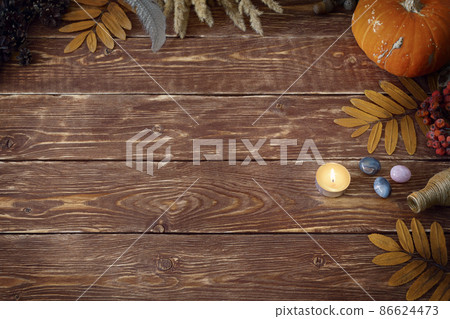 Autumn authentic layout on wooden backdrop with dry leaves, pumpkin, ashberry, agate gemstones, bottle, candle and feather, copy space, selective focus. 86624473
