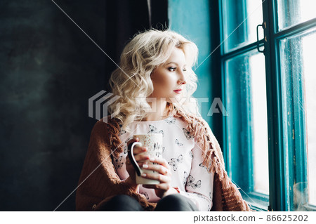 Pretty blonde on windowsill andl holding a cup in 86625202