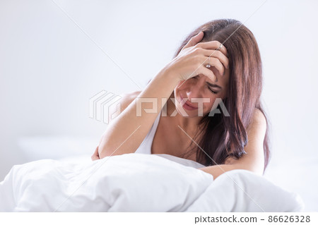 Woman wakes up in bed with severe migrene holding her head Woman wakes up in bed with severe migrene holding her head 86626328