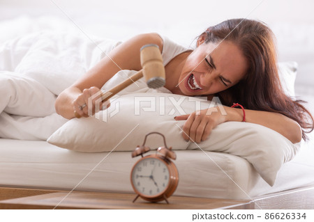 Brunette upset from the sound of the alarm clock is about to smash it with the hammer Brunette upset from the sound of the alarm clock is about to smash it with the hammer 86626334
