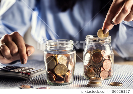 Detail of hands counting coins in two jars on a calculator Detail of hands counting coins in two jars on a calculator 86626337