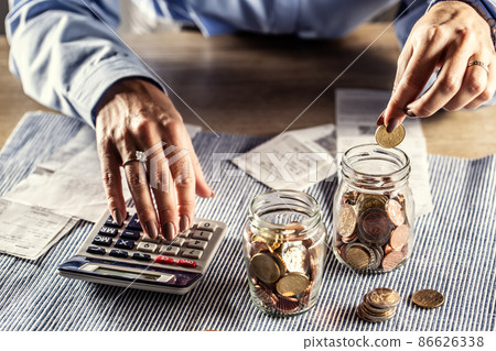 Counting bills and coins inside the jar while summing it up on a calculator Counting bills and coins inside the jar while summing it up on a calculator 86626338