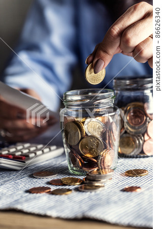 Putting 50 cents into a jar of euro coins by a woman counting bills Putting 50 cents into a jar of euro coins by a woman counting bills 86626340