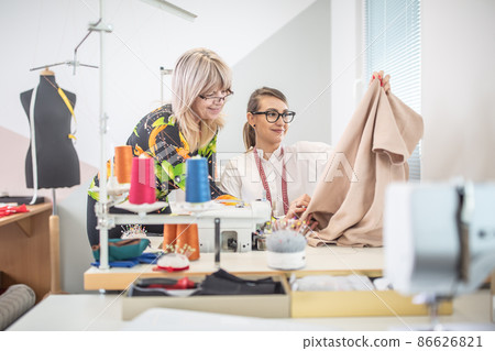 Positive working environment as two female tailors check the quality of their work in a small workshop Positive working environment as two female tailors check the quality of their work in a small workshop 86626821