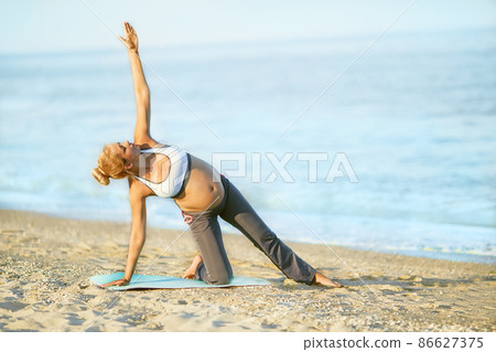 Pregnant woman doing yoga on the beach. Soft light. Beautiful girl with a swimsuit. Sea. Pregnant woman doing yoga on the beach. Soft light. Beautiful girl with a swimsuit. Sea. 86627375
