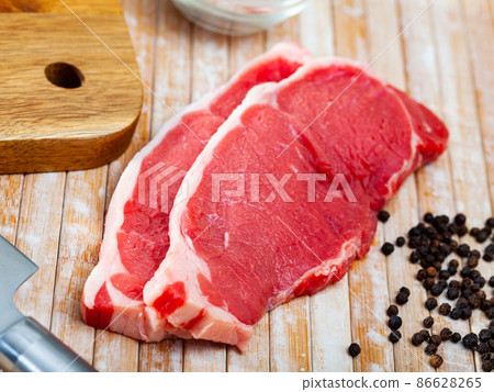 Raw beef steaks with condiments on wooden table 86628265