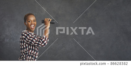 Wow, that's cool. Copy space banner background with studio portrait of happy smiling black woman holding binoculars, waiting and looking forward to big sale, bargain, special offer, clearance, blowout 86628382