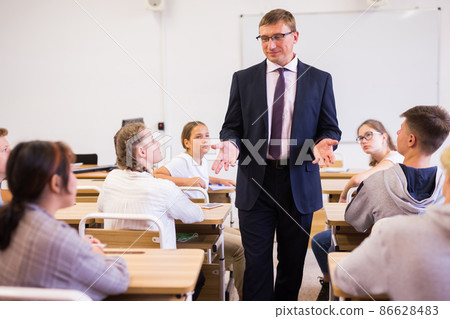 Male teacher lecturing to students at classroom Male teacher lecturing to students at classroom 86628483