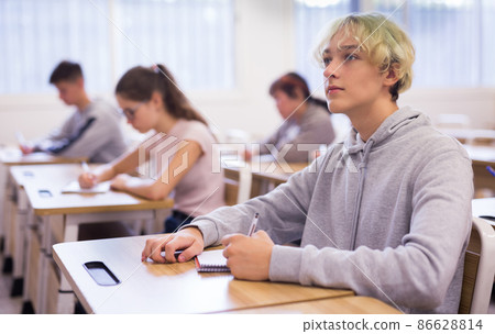 Teen boy sitting at desk in classroom 86628814