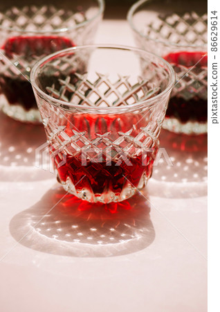 Red wine in a transparent glass with abstract shadows on pink background. Red wine in a transparent glass with abstract shadows on pink background. 86629614
