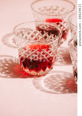 Red wine in a transparent glass with abstract shadows on pink background. Red wine in a transparent glass with abstract shadows on pink background. 86629615