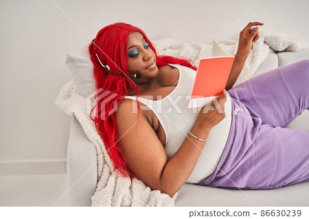 Multiracial woman wearing headset laying at the sofa and reading her notes while studying Multiracial woman wearing headset laying at the sofa and reading her notes while studying 86630239