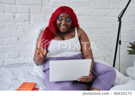 Smiling woman looking at computer while sitting on white bed Smiling woman looking at computer while sitting on white bed 86630273