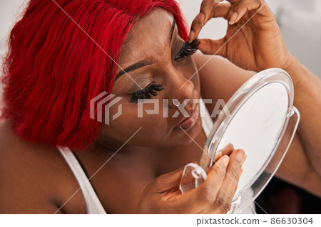 Woman with red hair putting lushes her eyes and preparing creative makeup while sitting at the sofa 86630304