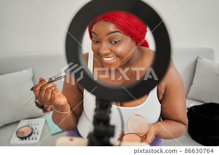 Multiracial woman blogger is preparing make up and using cosmetics in front of the smartphone 86630764