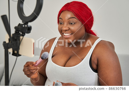 Multiracial woman preparing applying blush on her chicks while broadcasting make up tutorial Multiracial woman preparing applying blush on her chicks while broadcasting make up tutorial 86630766