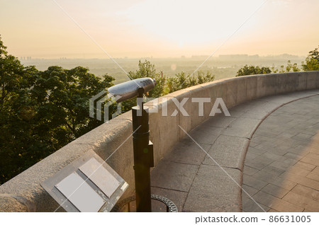 Tourist coin telescope. Metal stationary binoculars standing on a high hill on the viewpoint, for observing the nature of a beautiful old historic city overlooking the river 86631005