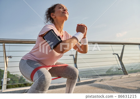 Female athlete exercising with elastic band on the city bridge. Sports woman doing body weight training outdoor early in the morning on a beautiful sunny day. Sport, active healthy lifestyle concept Female athlete exercising with elastic band on the city bridge. Sports woman doing body weight training outdoor early in the morning on a beautiful sunny day. Sport, active healthy lifestyle concept 86631215