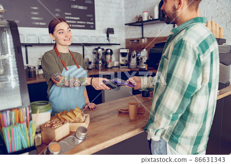Young man paying for coffee with smartphone in cafe Young man paying for coffee with smartphone in cafe 86631343