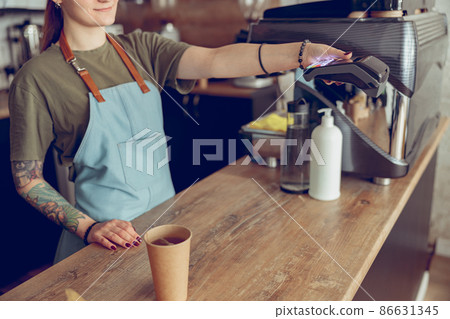 Female barista using terminal for contactless payment in coffee shop Female barista using terminal for contactless payment in coffee shop 86631345