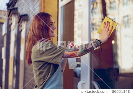 Joyful young woman cleaning window outside coffeehouse Joyful young woman cleaning window outside coffeehouse 86631348