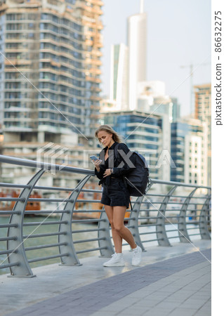 A young woman with a smartphone is standing on the embankment. The concept of online communication A young woman with a smartphone is standing on the embankment. The concept of online communication 86632275