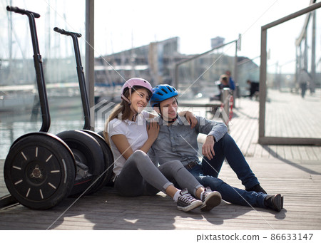 young couple guy and girl are walking on the segway along the board paved promenade in the port of a European city young couple guy and girl are walking on the segway along the board paved promenade in the port of a European city 86633147