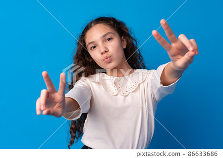 Young teen girl showing a peace symbol with fingers against blue background Young teen girl showing a peace symbol with fingers against blue background 86633686