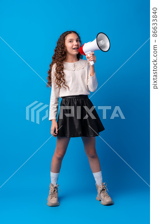 Cute schoolgirl holding megaphone against blue background 86633840