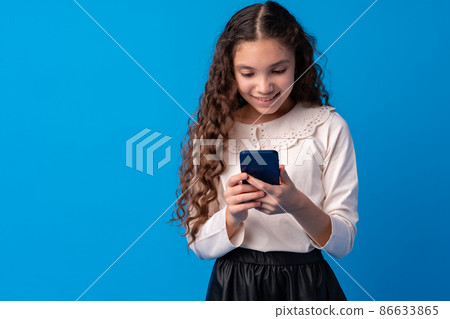Little girl using mobile phone.against blue background Little girl using mobile phone.against blue background 86633865