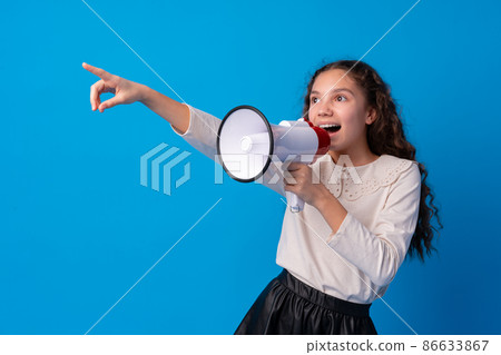 Cute schoolgirl holding megaphone against blue background Cute schoolgirl holding megaphone against blue background 86633867