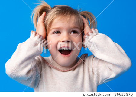Beautiful little girl with hands on head being delighted and shocked over blue background. 86633870