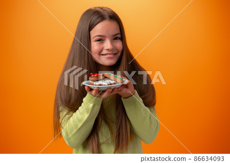 Portrait of little girl holding plate with cookies against orange background 86634093